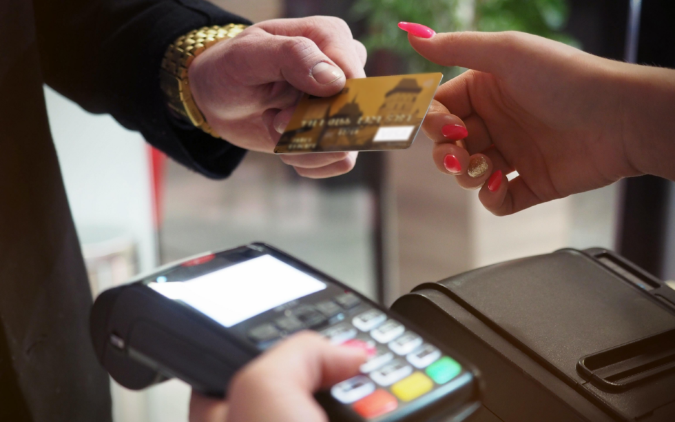 duas mãos, uma recebendo um cartão de crédito para realizar um pagamento em uma maquineta