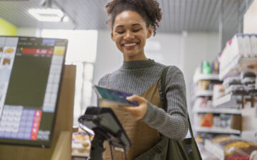 Imagem de uma mulher sorridente efetuando o pagamento digital pelo celular no caixa da loja.