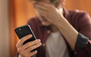 Um homem preocupado com uma mão na cabeça e outra no celular depois de sofrer o golpe da Serasa.