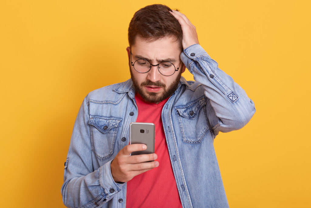 Um homem olhando para o celular depois de sofrer o golpe da Serasa.