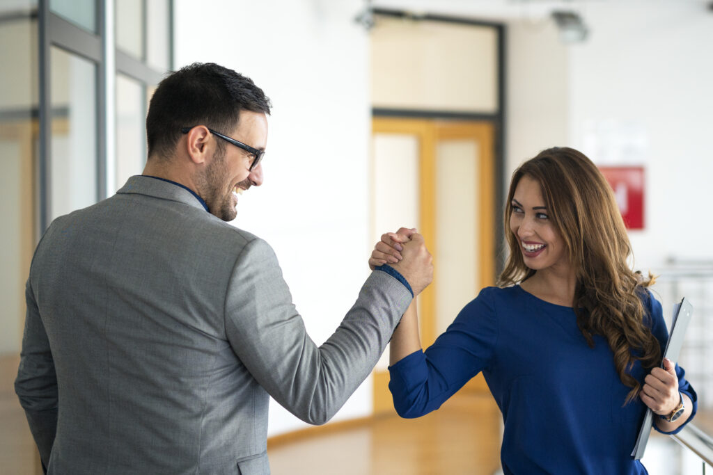 Parceiros de trabalho se cumprimentam e sorriem em tom comemorativo.