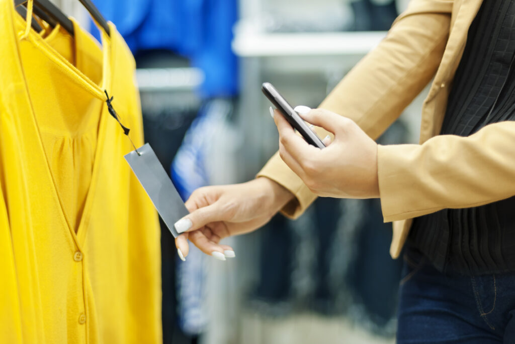 Imagem de uma mulher escaneando, com o celular, o QR code na etiqueta de uma blusa.