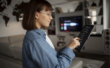 Imagem de uma mulher utilizando um ipad para acessar uma smart TV.