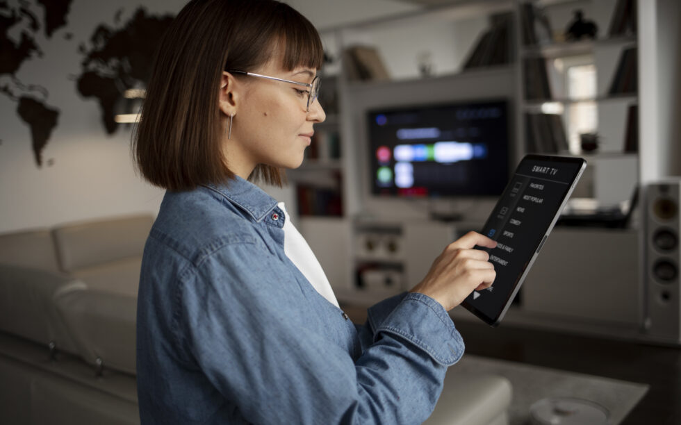 Imagem de uma mulher utilizando um ipad para acessar uma smart TV.
